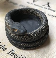 two small black pots sitting on top of a table next to each other, one with a lizard in it's mouth