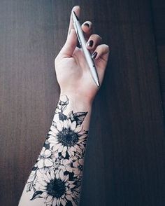 a woman's arm with flowers on it and a pen in the other hand