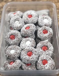 a plastic container filled with lots of donuts covered in powdered sugar and cherries