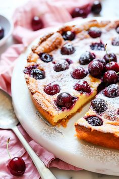 a cake with cherries and powdered sugar is on a plate next to a fork