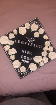 a decorated graduation cap sitting on top of a pink bed sheet covered in white roses