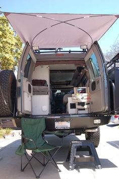 the back end of an rv with its doors open and two chairs in front of it