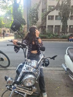 a woman sitting on top of a motorcycle talking on a cell phone next to a street