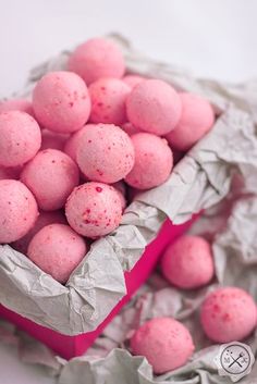 there is a pink box filled with small round candy balls on top of crumpled paper