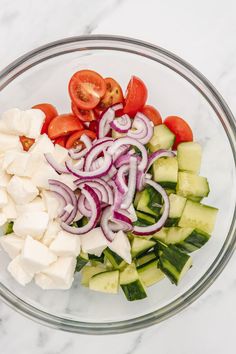 a glass bowl filled with cucumber, tomatoes and onions on top of a marble counter