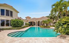 a large pool in front of a house with palm trees around it and a bench on the side