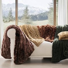 a white couch with blankets on it in front of a large window and mountain view