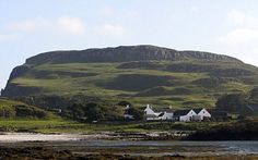 some houses are on the side of a hill near water and grass with mountains in the background