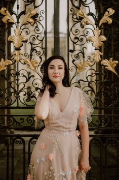 a woman standing in front of a gate wearing a pink dress with flowers on it