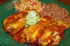 a green plate topped with enchiladas, beans and rice