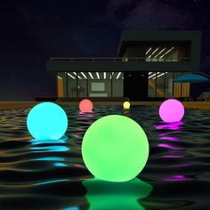 several glowing balls floating in the water near a building and beach umbrellas at night