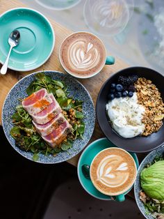 several plates of food and cups of coffee on a wooden table with utensils