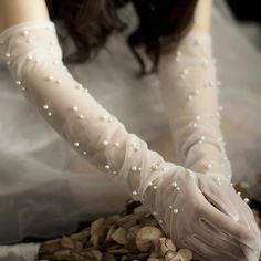 a woman wearing white gloves and pearls on her hands