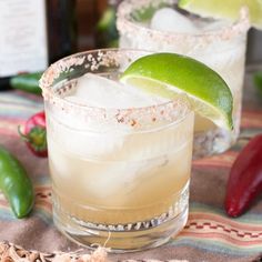 two margaritas sitting on top of a table next to peppers