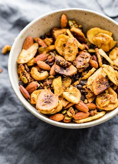 a bowl filled with nuts and bananas on top of a gray table cloth next to a spoon