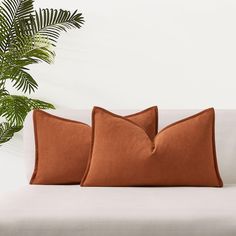 two orange pillows sitting on top of a white couch next to a potted plant