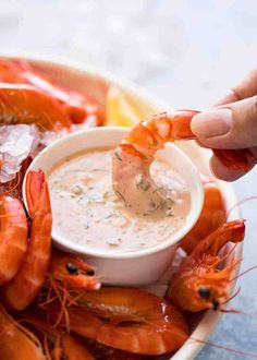 a person dipping shrimp into a bowl of dip with lemon wedges on the side