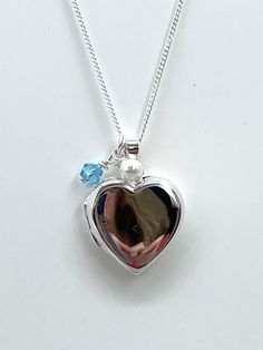 "A heart-shaped Sterling Silver Photo Locket hangs alongside a Swarovski pearl and a 'something blue' crystal. This beautiful gift for the Bride is an elegant nod to the something blue tradition and a lovely way to keep special photographs close to the heart. An 18mm sterling silver heart-shaped photo locket opens for you to add up to two photographs and hung from a 16\"-18\" adjustable sterling silver chain. Choose from an ivory or cream Swarovski pearl to hang next to the pretty blue Swarovski crystal.   Your gift will be presented in an elegant card wallet printed with the message of your choice and tied with a silver-grey satin ribbon.  Choose from: A: Walking with You on your Wedding Day B. Always with you C. With you every step of the way D. Forever by your side E. Your own wording L Heart-shaped Jewelry For Mother's Day, Wedding Heart Charm Locket Necklace, Double Heart Locket Necklace For Wedding And Mother's Day, Blue Heart Pendant Keepsake Jewelry, Blue Engraved Jewelry For Keepsake, Blue Locket Necklace For Wedding, Wedding Round Locket Necklace With Heart Charm, Wedding Heart Cut Locket Necklace, Heart Cut Locket Necklace For Wedding