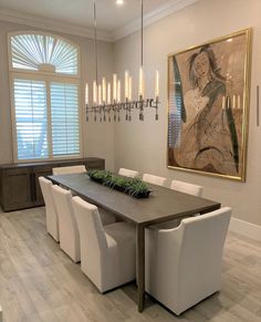 a dining room table with white chairs and a painting on the wall