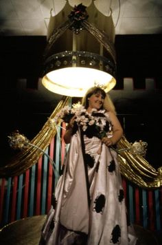 a woman in a white and black dress standing next to a chandelier with flowers on it