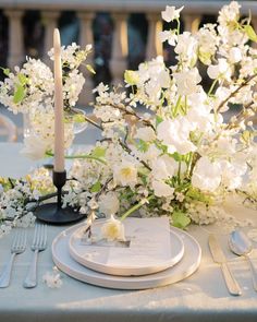 the table is set with white flowers and silverware, candles and napkins on it