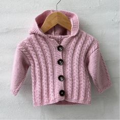 a pink knitted sweater hanging on a wooden hanger next to a white wall