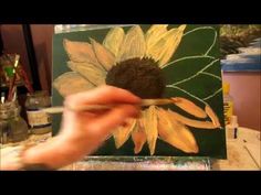 someone is painting a sunflower on a canvas