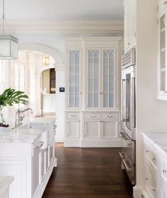 a large kitchen with white cabinets and wood flooring, along with an arched doorway leading to the dining room