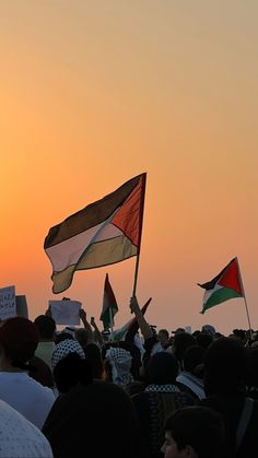 many people are holding flags and waving their hands in front of an orange sky at sunset