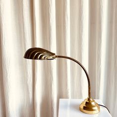 a gold lamp sitting on top of a white table next to a curtained window