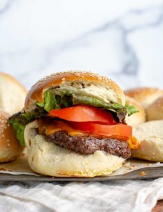 a hamburger with lettuce, tomato and cheese on it next to bagels