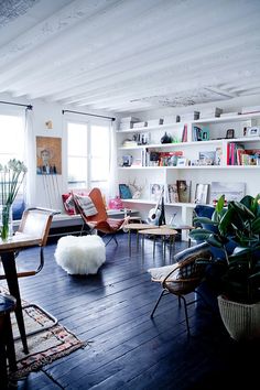 a living room filled with lots of furniture and plants on top of a hard wood floor