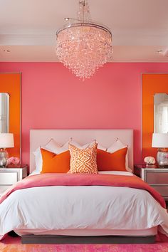 a bedroom with pink walls and white bedding, chandelier and orange pillows