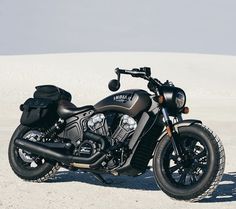 a black motorcycle parked on top of a sandy beach next to a white sand dune