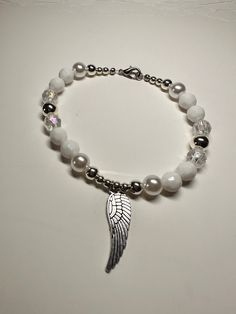 "This is a beautiful OOAK handmade beaded bracelet with an Angel wing charm. The pearl beads really make the silver and clear beads shine! Very pretty white and silver color with  clear beads for accent on a stretchy elastic but has a clasp as well. Also features an Angel wing charm. Will fit a 7\" wrist. Picture taken in different lighting to show how it looks under different settings. We offer free shipping on all of our items! If you are interested in a certain color combination, please send Silver Beaded Pearl Stretch Bracelet, Silver Pearl Stretch Bracelet Gift, Silver Pearl Stretch Bracelet As Gift, Silver Pearl Stretch Bracelet For Gift, White Angel Wings Jewelry As Gift, White Stretch Bracelet With Silver Beads As Gift, Angel Accessories, Angel Wing Bracelet, Homemade Necklaces