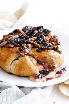 a white plate topped with a pastry covered in nuts and raisins on top of it