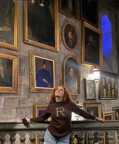 a woman is standing in front of some portraits on the wall with her arms outstretched