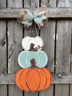 three pumpkins are hanging on a wooden fence with a bow in the middle and one is painted orange, white and blue