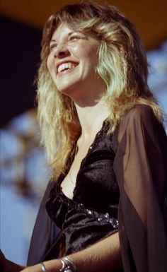 a woman with blonde hair smiling and wearing a black dress