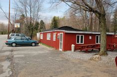 a car parked in front of a red building with picnic tables and benches next to it