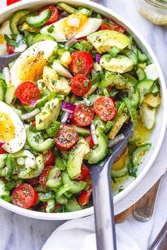 a bowl filled with cucumber, tomatoes and hard boiled eggs on top of a table