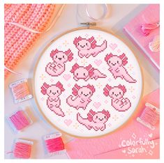 a cross stitch pattern with pink yarn and other crafting supplies on the table next to it