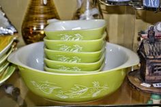 four green bowls are stacked on top of each other in front of some decorative items