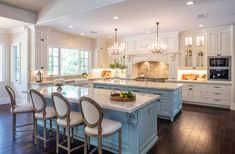 a large kitchen with an island in the middle and chairs at the end, surrounded by white cabinetry