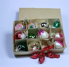 an open box filled with assorted ornaments on top of a white table next to red bows