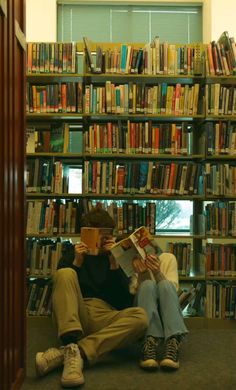 two people sitting on the floor in front of a bookshelf full of books