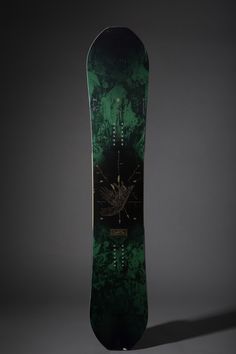 a green skateboard with black and gold designs on the bottom half, against a gray background