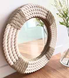 a white rope mirror sitting on top of a wooden floor next to a vase with flowers