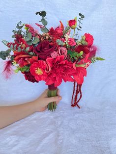 a woman holding a bouquet of red flowers and greenery on a white background,