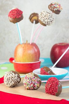 apples and chocolate covered strawberries in bowls on a table with candy sticks sticking out of them